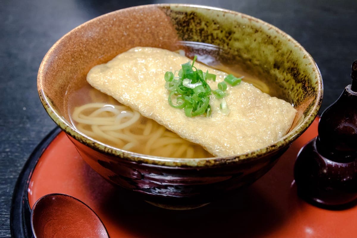 Kitsune udon: udon in broth with a sheet of fried tofu and green onion