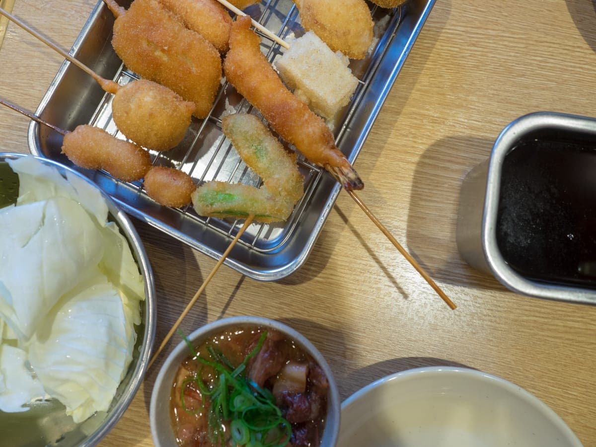 Kushikatsu skewers on a tray, with cabbage and dipping sauce