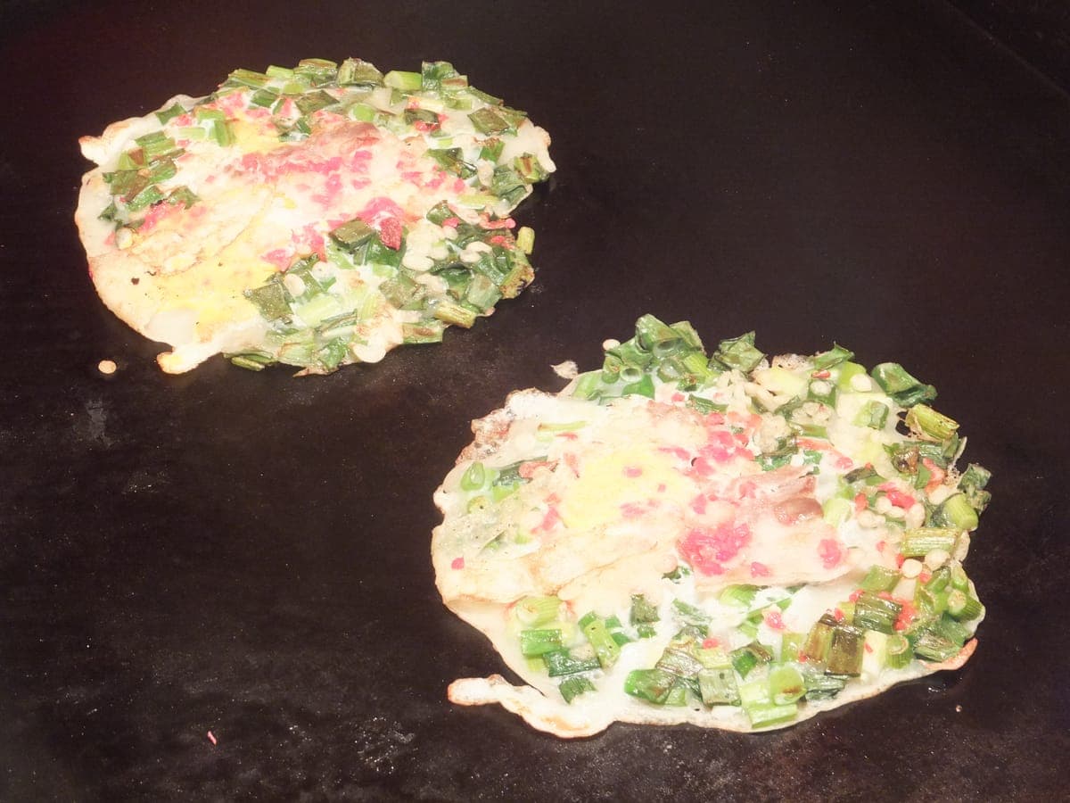 Negiyaki cooking on a griddle, covered with green onion